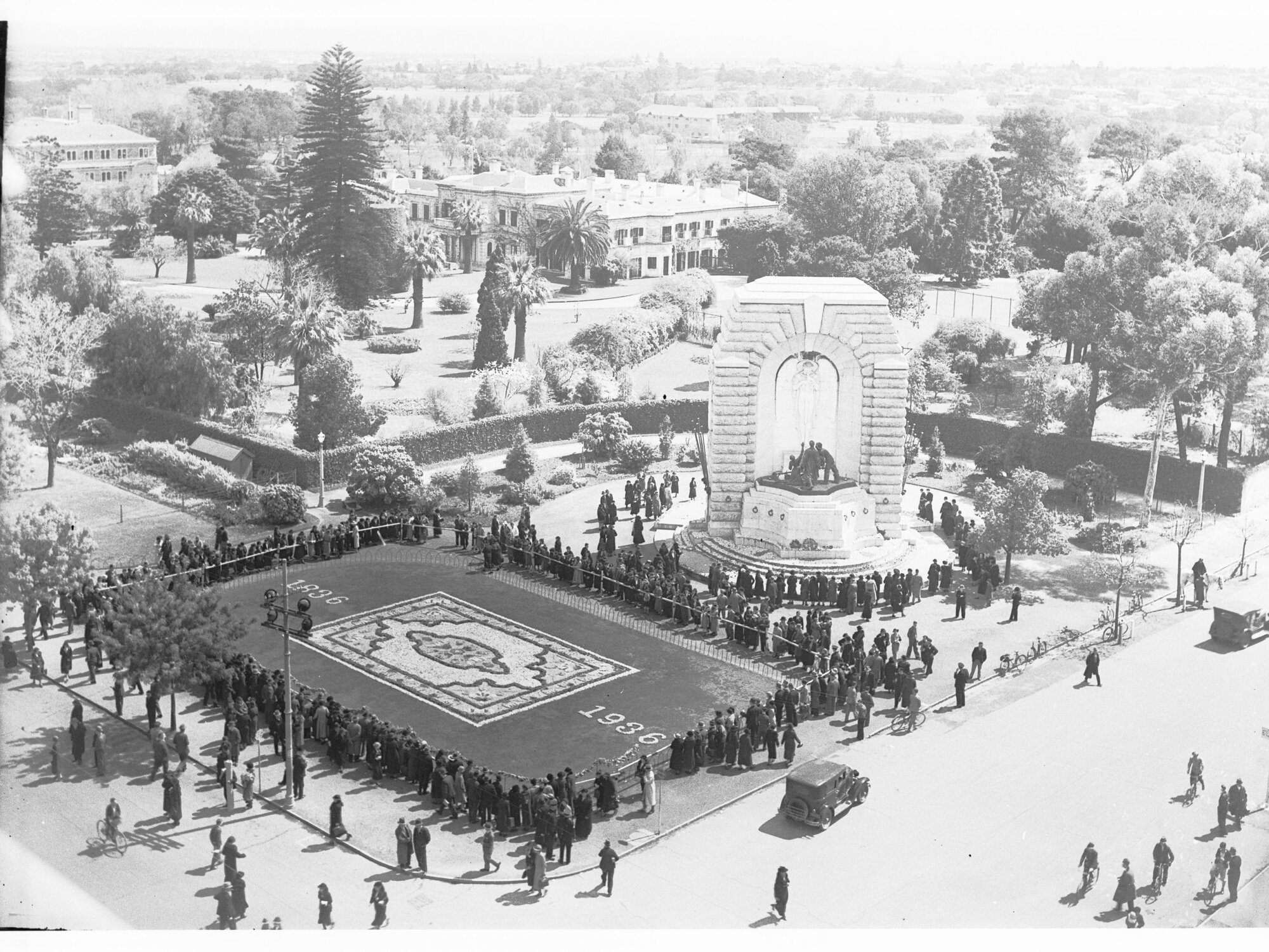 Crowd inspecting the floral carpet and flowers on the War Memorial at corner of Kintore Avenue and North Terrace - Flower Day 1936