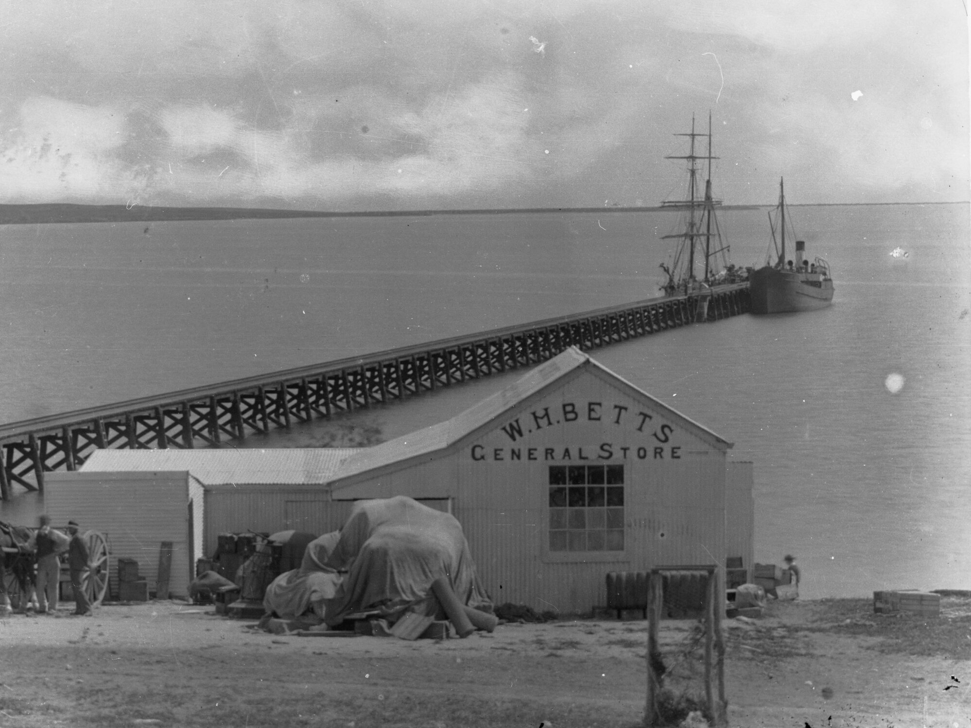 Coastal view showing jetty and ships berthed at end of jetty.  W.H. Betts general store.