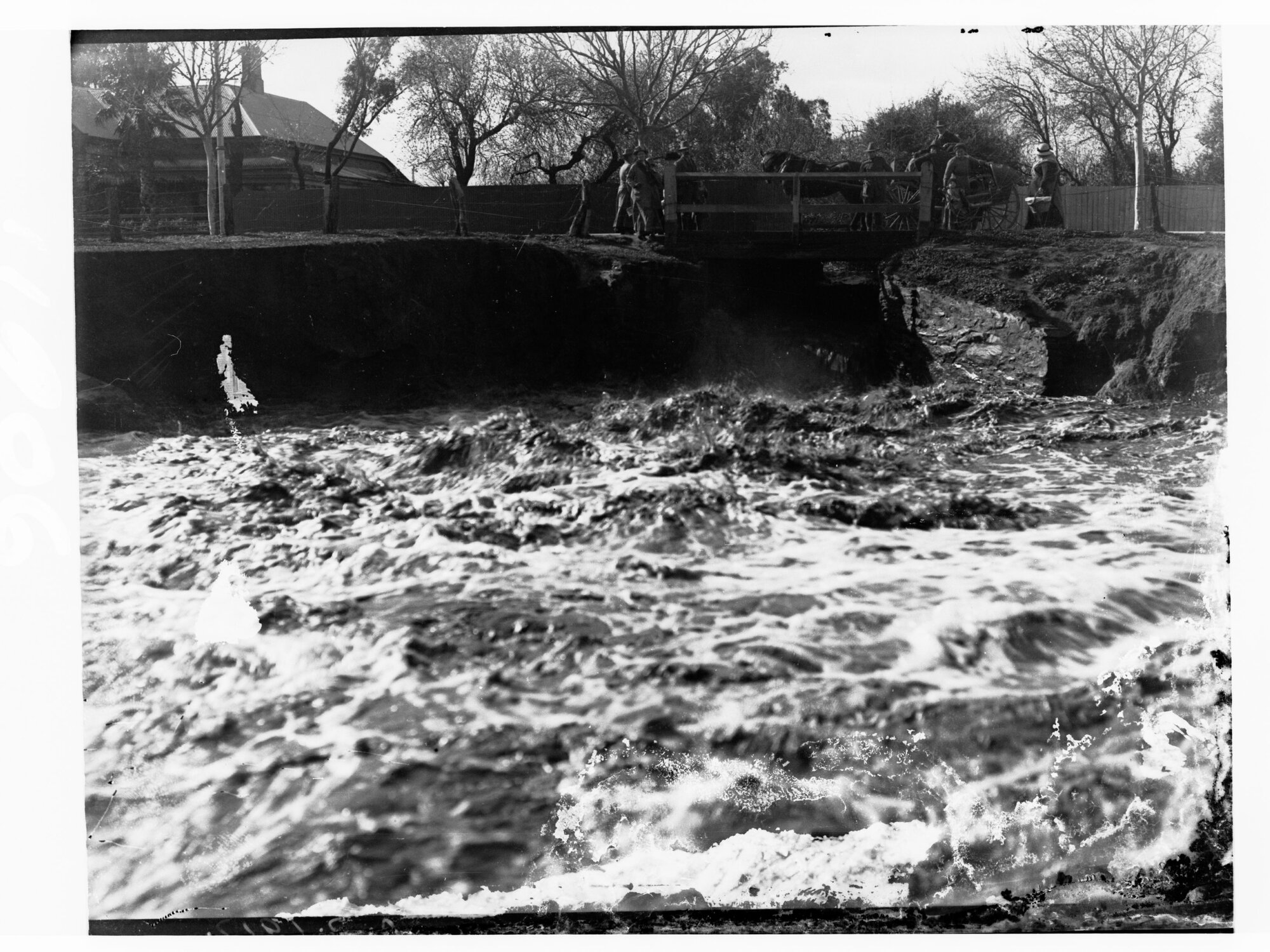 People standing on a bridge looking at a raging river during floods