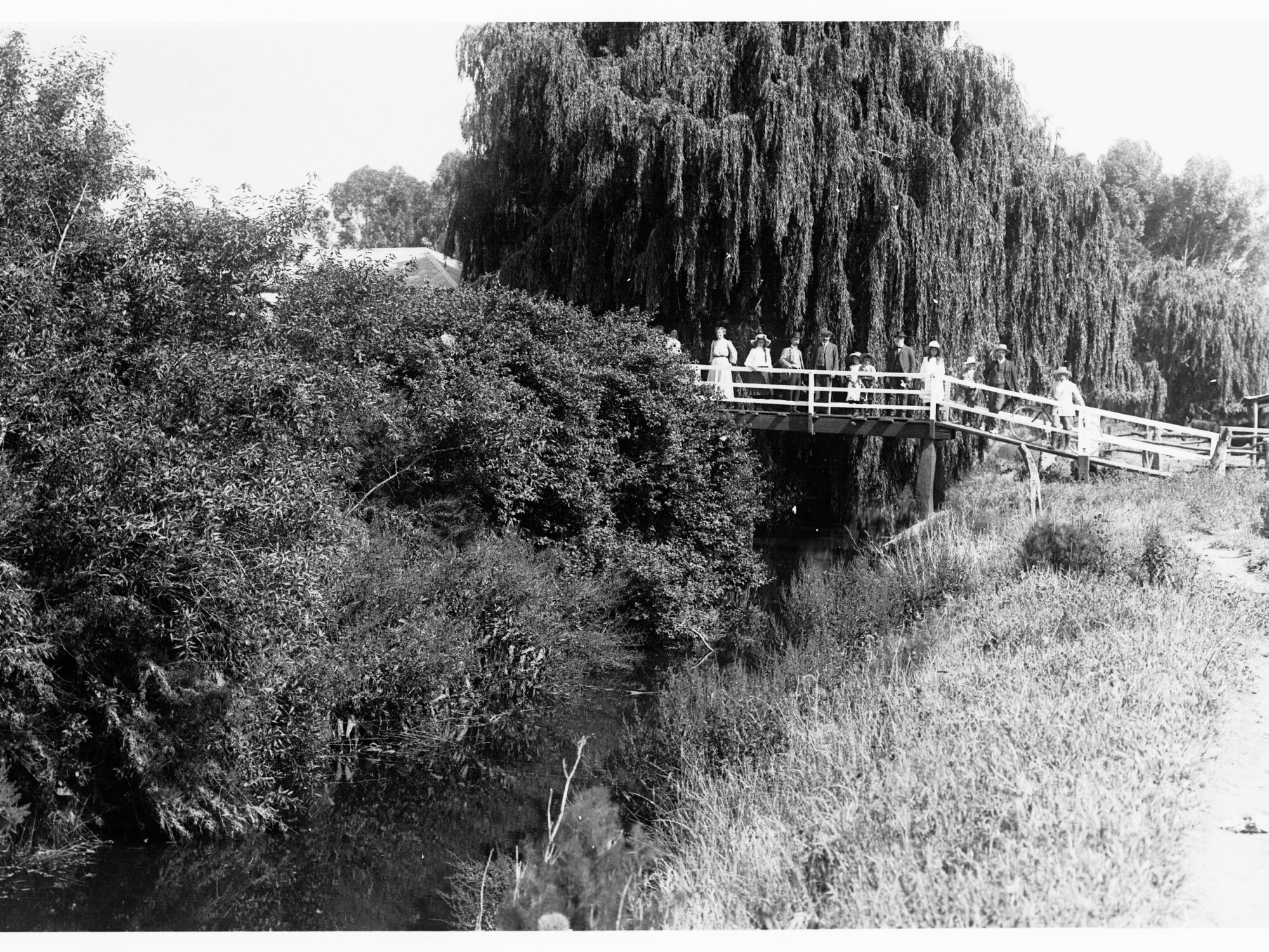 Men, women and children standing on foot bridge over a creek
