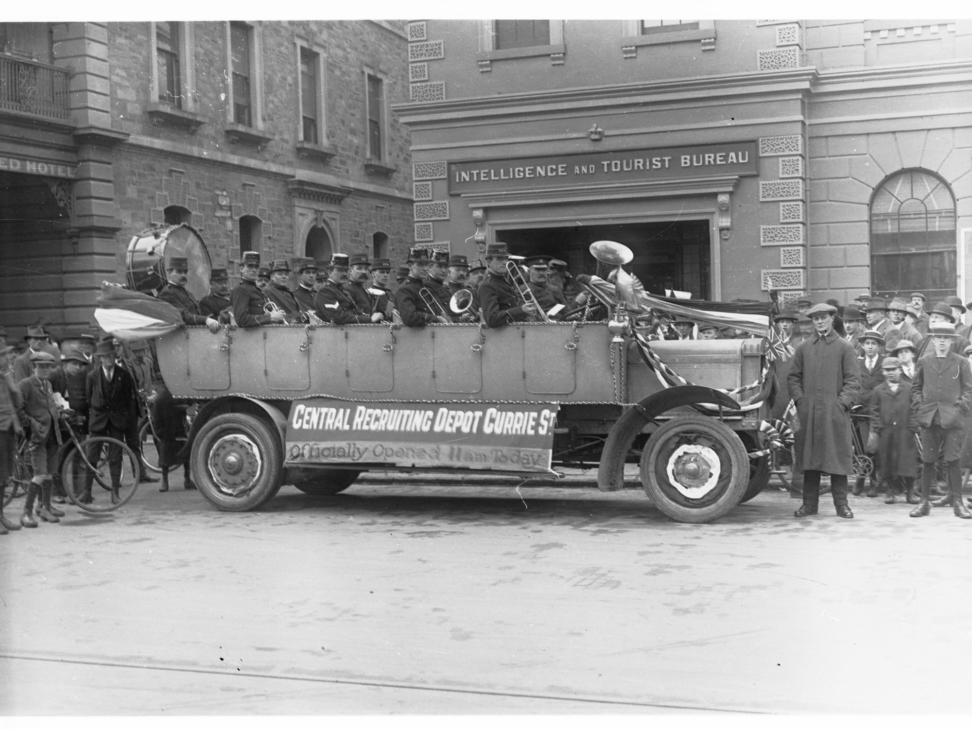 Decorated Charabanc outside Intelligence and Tourist Bureau, King William Street - band members holding their instruments are in car for the official opening of Central Recruiting Depot on Currie Street.  (Charabanc is displaying sign which says "Central 