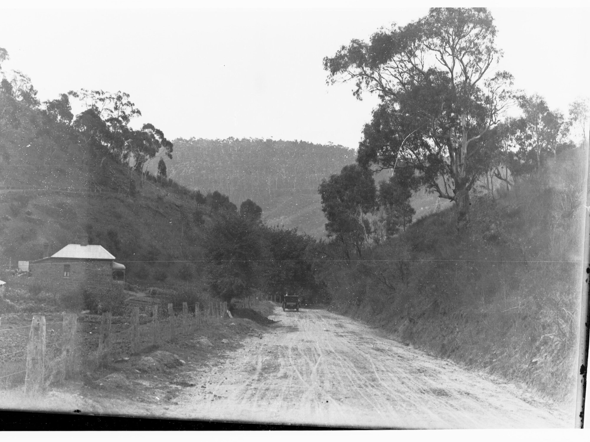 View in Mount Lofty Range showing automobile on dirt road and a cottage