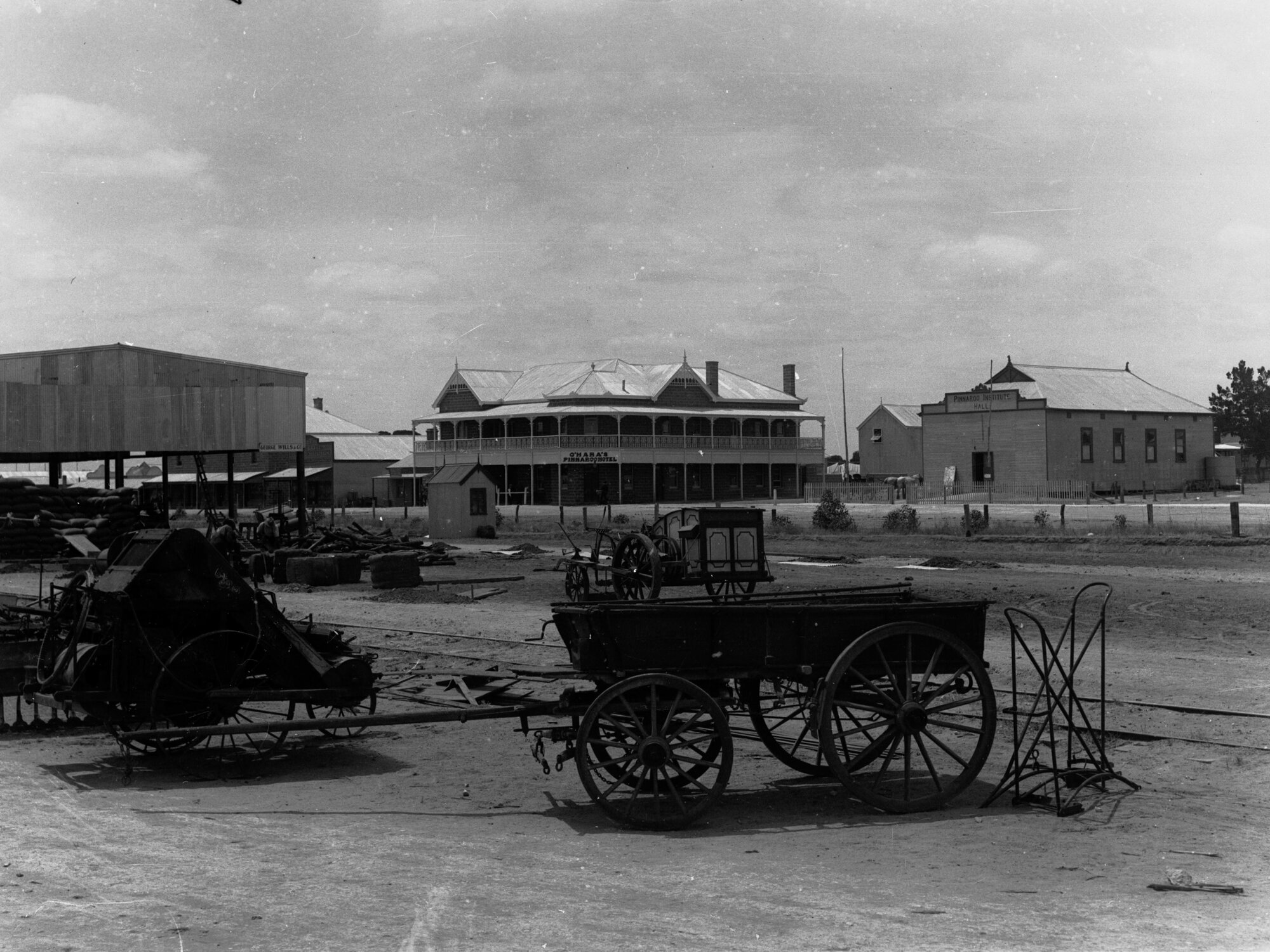 Carting wheat at Pinnaroo, showing carts and machinery, O'Hara's Pinnaroo Hotel and Pinnaroo institute in the background
