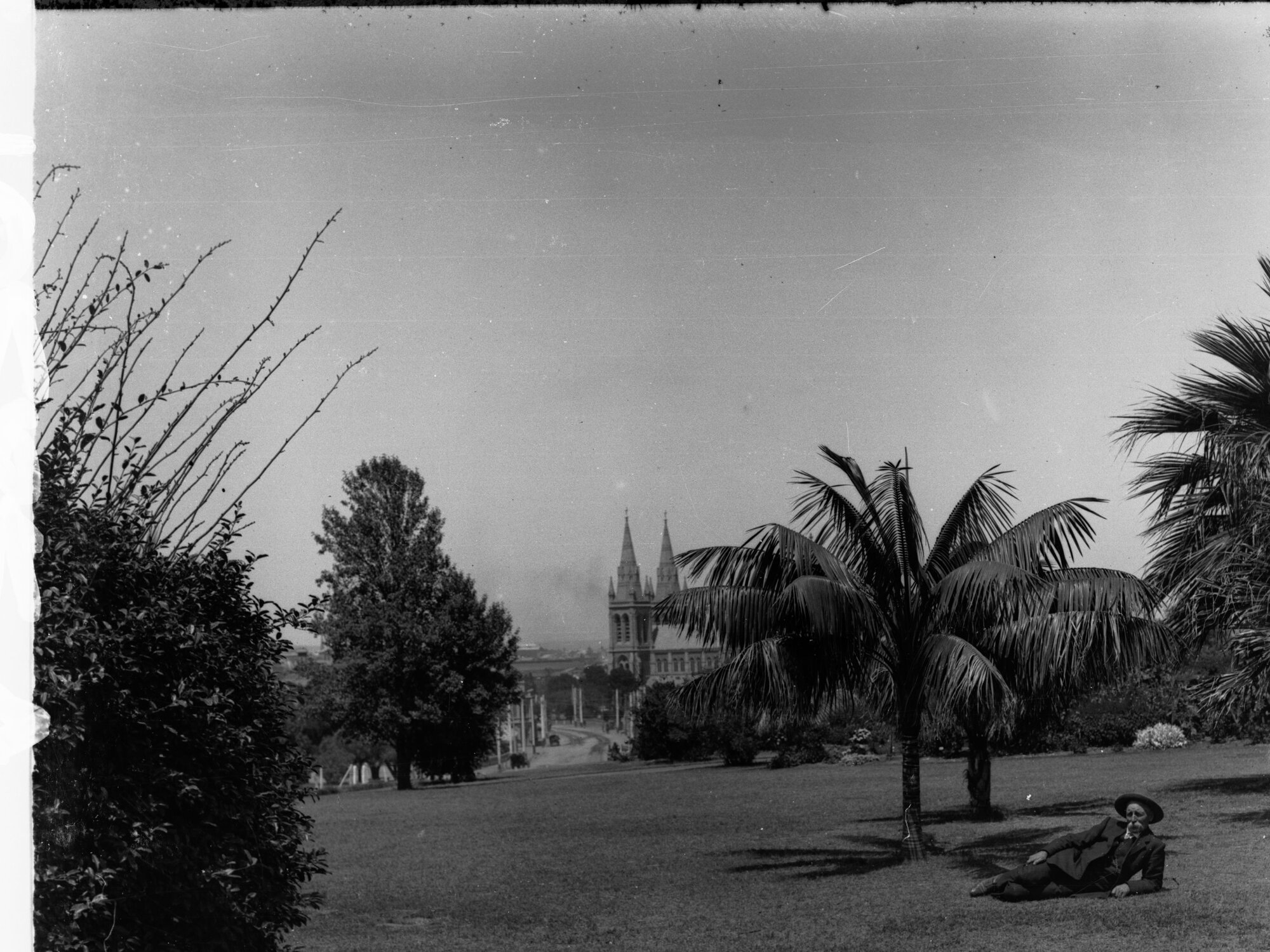 Brougham Place, North Adelaide with St Peters Cathedral in the background.  View across garden, man lying on grass.