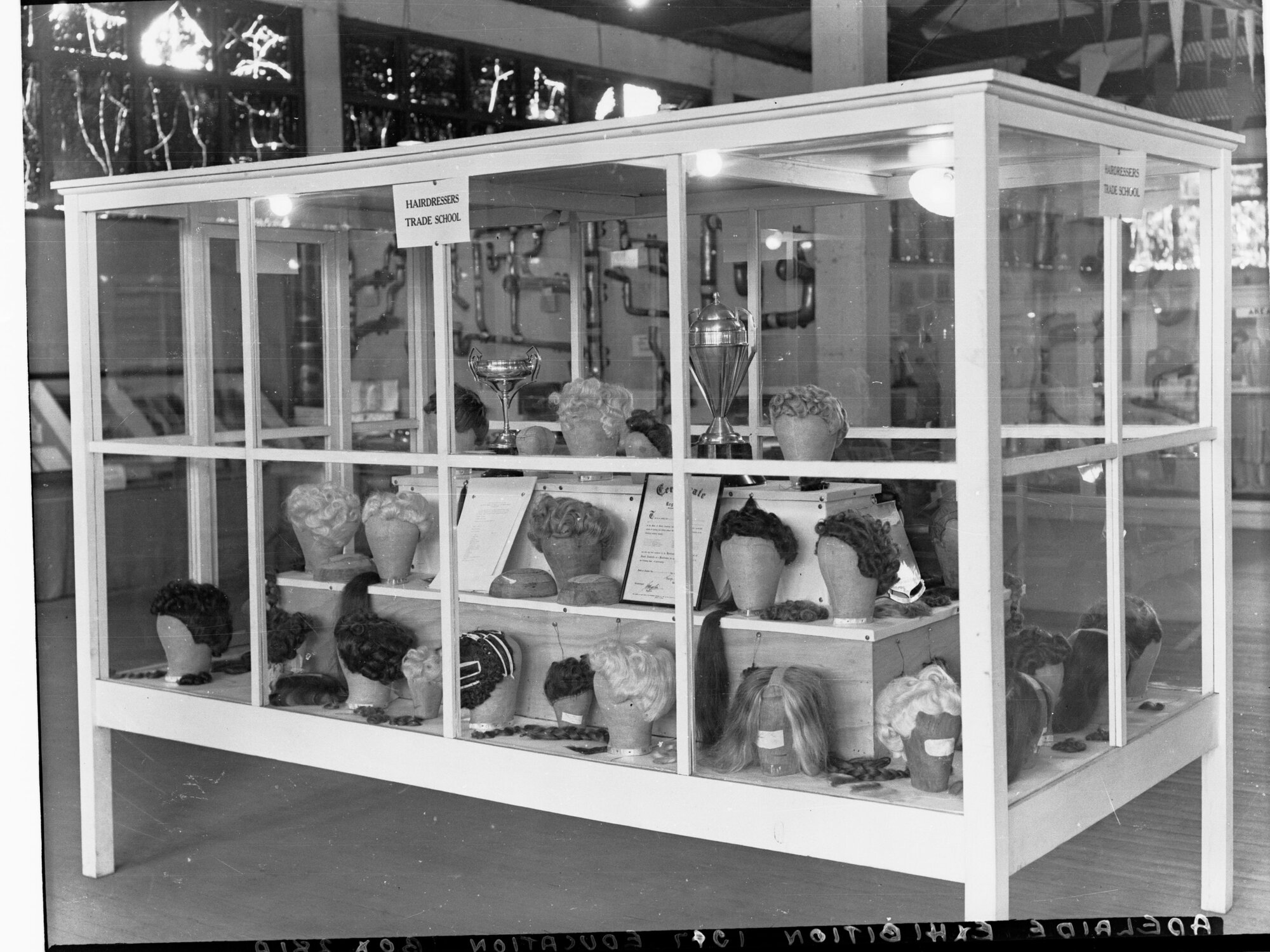 Hair Dressers Trade School Exhibition showing wigs in a glass cabinet