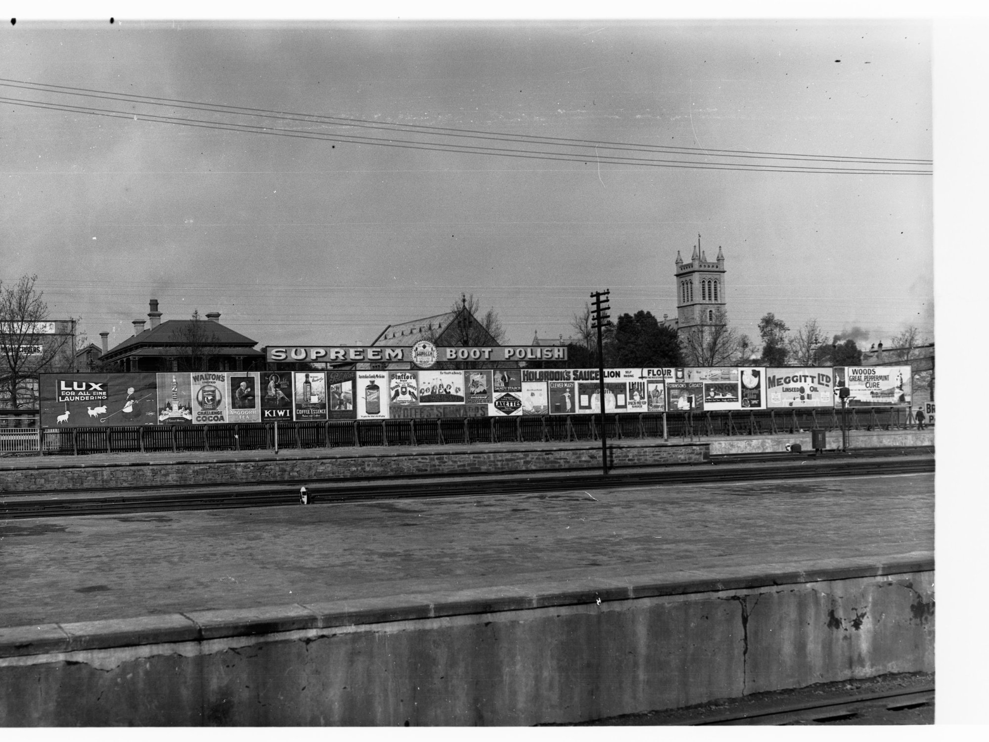 Billboards on Adelaide Railway Station Platform looking south over North Terrace, Trinity church in background