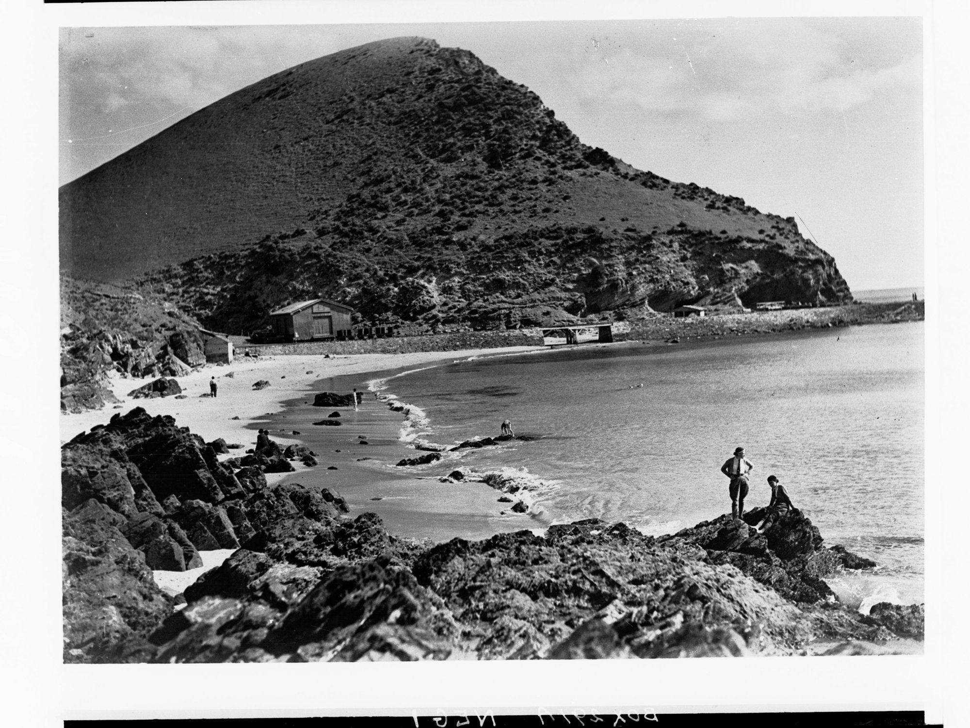 Coastal view showing boat sheds in the distance and people on rocks - Second Valley