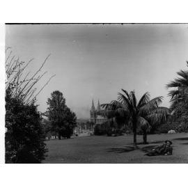 Brougham Place, North Adelaide with St Peters Cathedral in the background.  View across garden, man lying on grass.