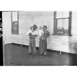 Man and woman standing in front of a building - both the man and woman are holding a young child