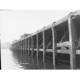 No. 2 Quay at Port Adelaide - view of underside of wharf - building in background W R Cave & Son, and man fishing