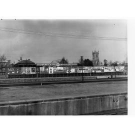 Billboards on Adelaide Railway Station Platform looking south over North Terrace, Trinity church in background