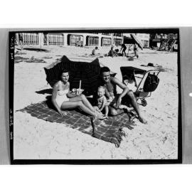 Henley Beach =- Man, woman and baby sitting on beach under umbrella