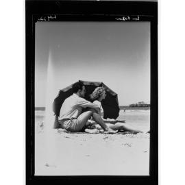Man and woman sitting on beach under umbrella